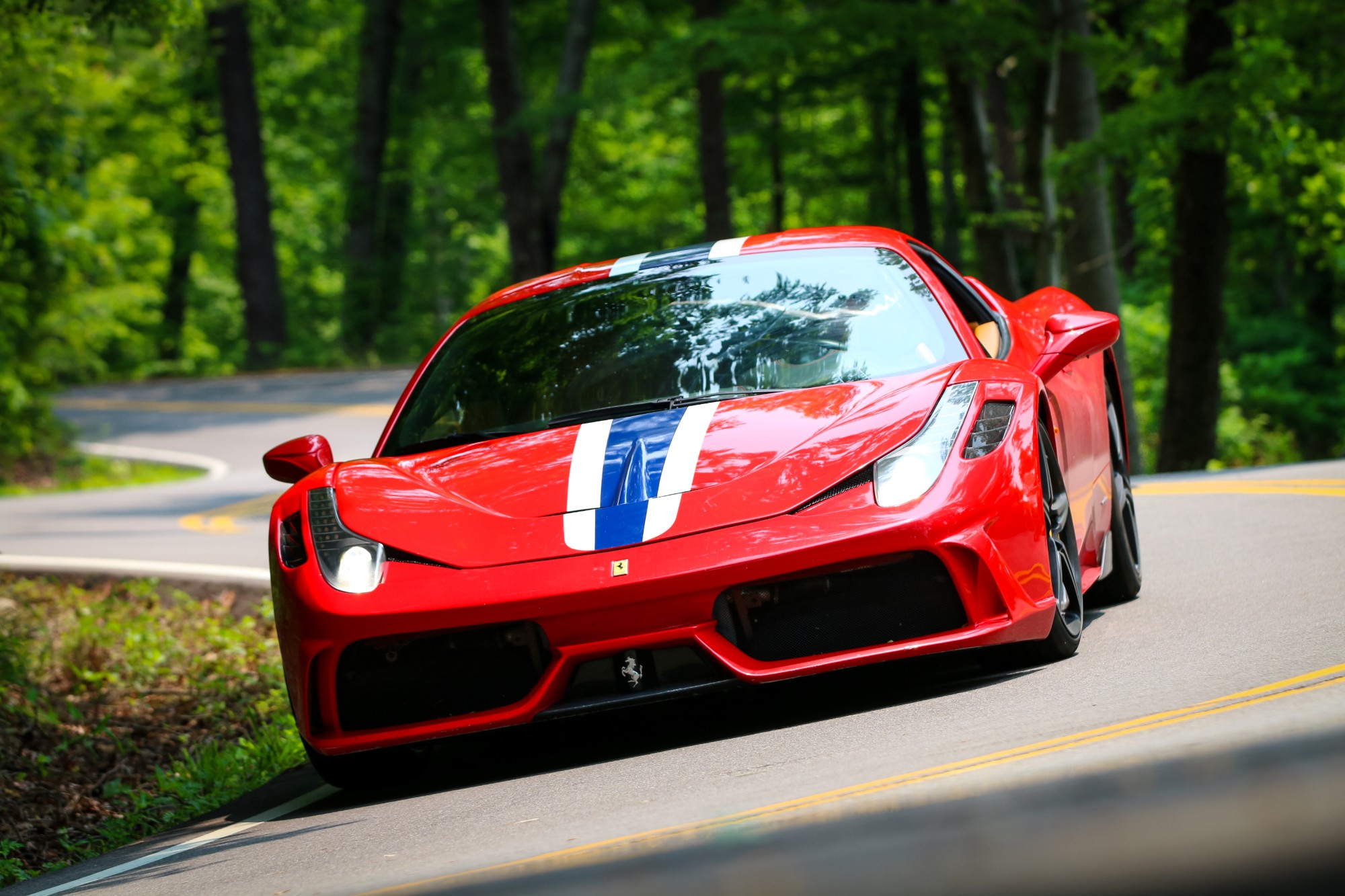 Red Ferrari 458 Speciale with white and blue stripes taking a bend on a wooded back road