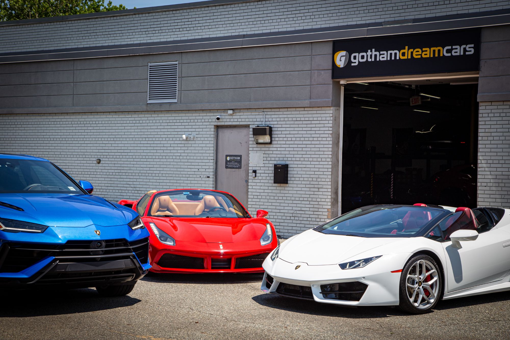 Our Teaneck garage under the Gotham Dream Cars sign, a blue Lamborghini Urus, a red Ferrari 488 Spider and a white Lamborghini Huracán Spyder parked out front