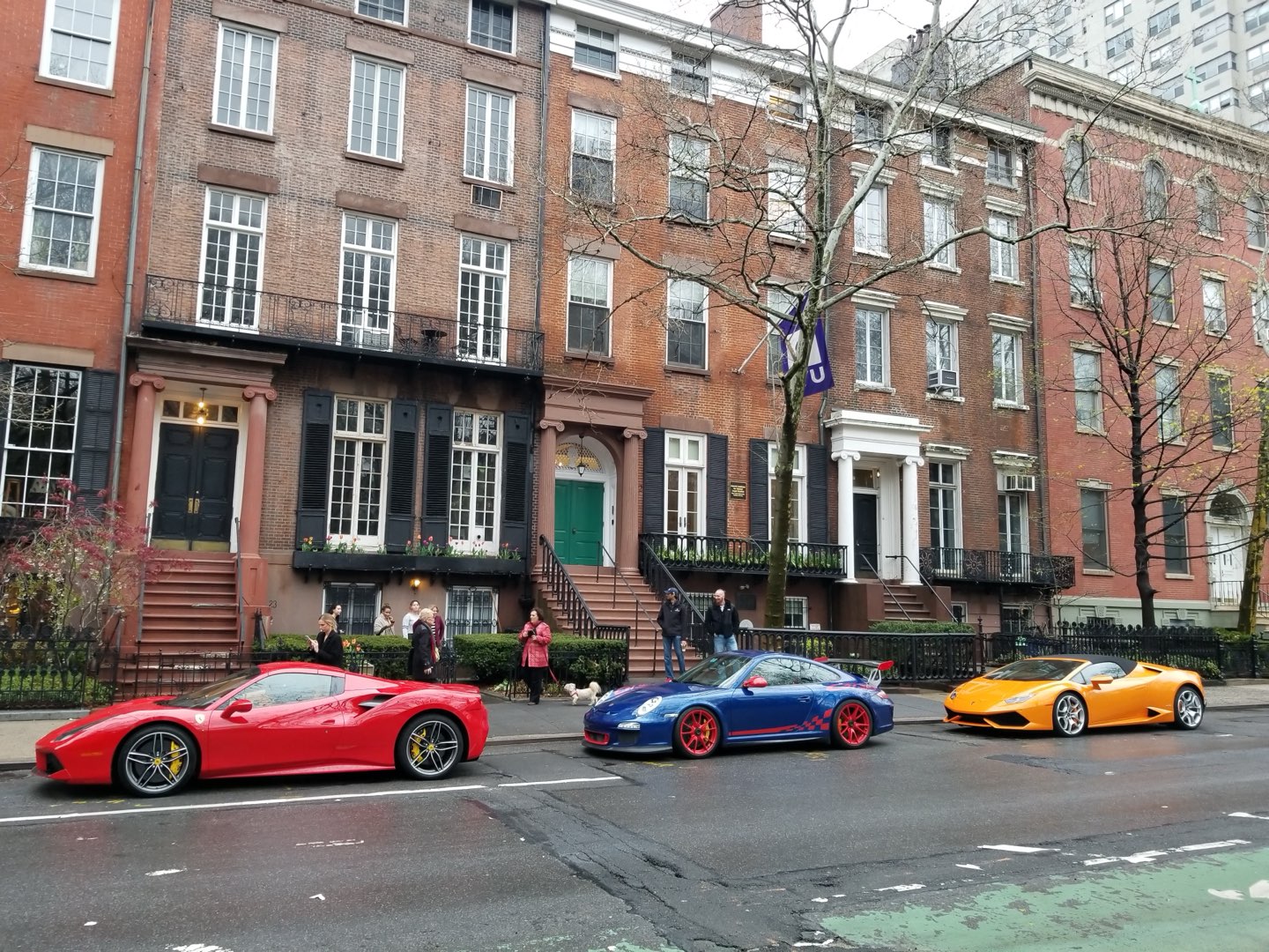 A red Ferrari, a blue Lamborghini and an orange Lamborghini parked along a row of brick townhouses in New York